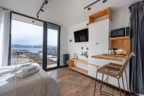 Coastal retreat bedroom opens to a quiet sea-view balcony under overcast skies, off-season calm and solitude.