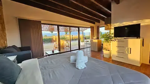 Empty lakeside hotel suite at sunrise, neatly made bed with towels, open terrace doors overlooking calm water in off-season.