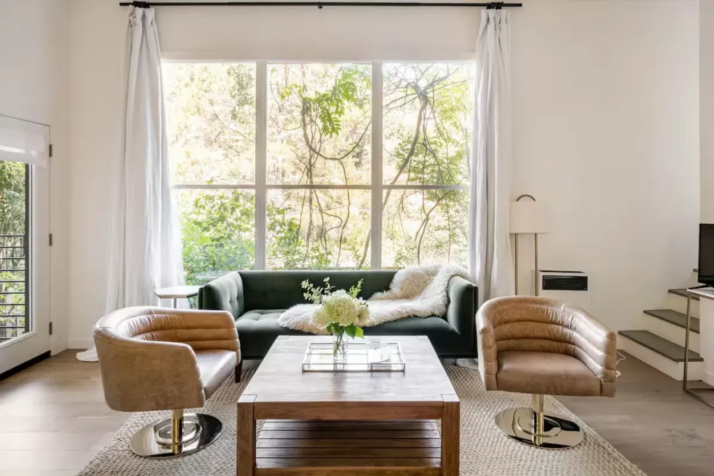 Off-season forest vacation rental living room with leather chairs, green sofa & coffee table by sunlit window.