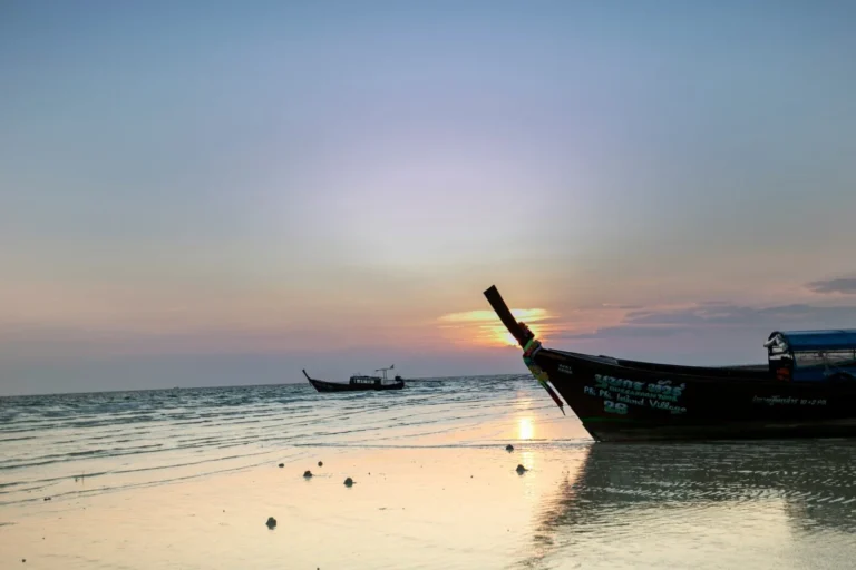 Tranquil beach scene at sunset with fishing boats and gentle waves, highlighting an off-season, serene atmosphere