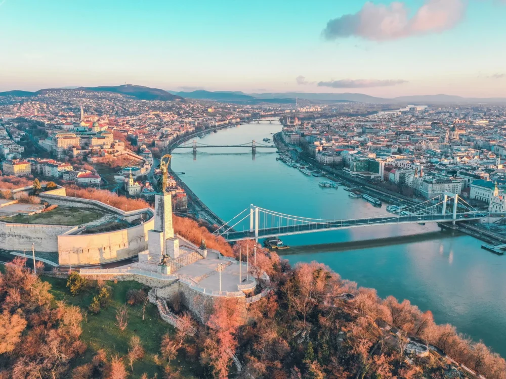 An aerial view of Budapest with the Danube River and bridges, under a clear sky.