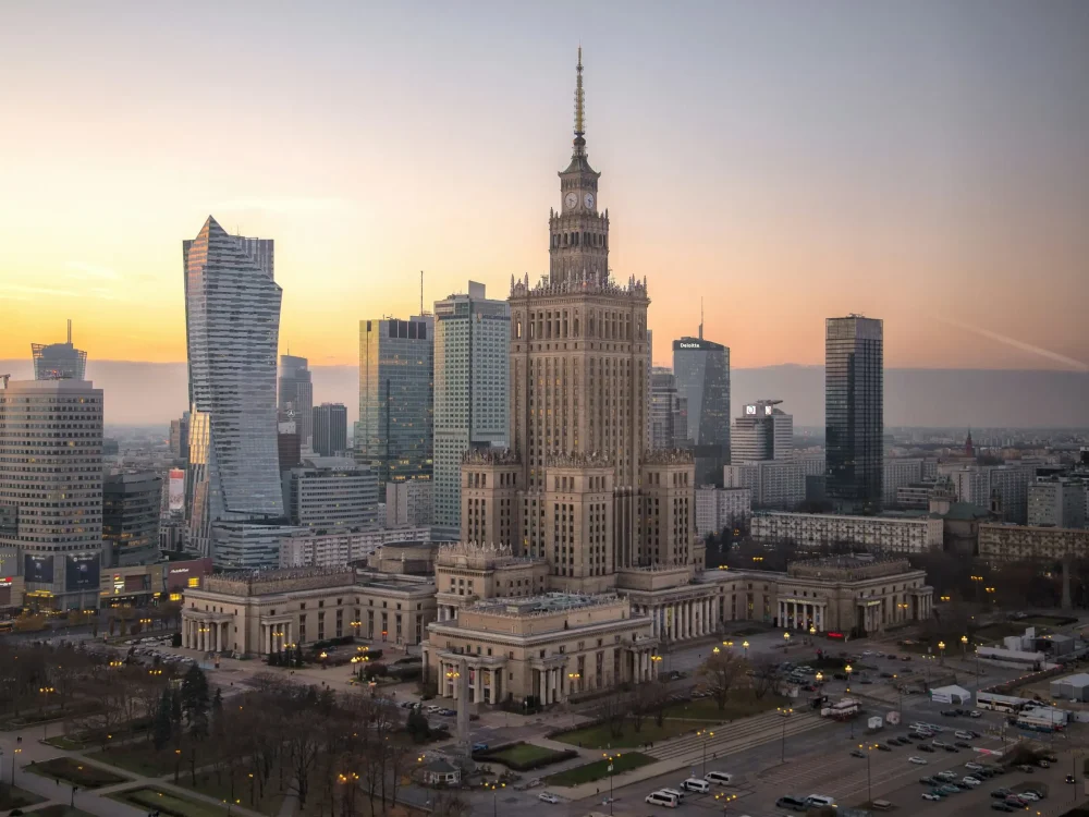 An aerial view of the Warsaw skyline at dusk, featuring the Palace of Culture and Science.