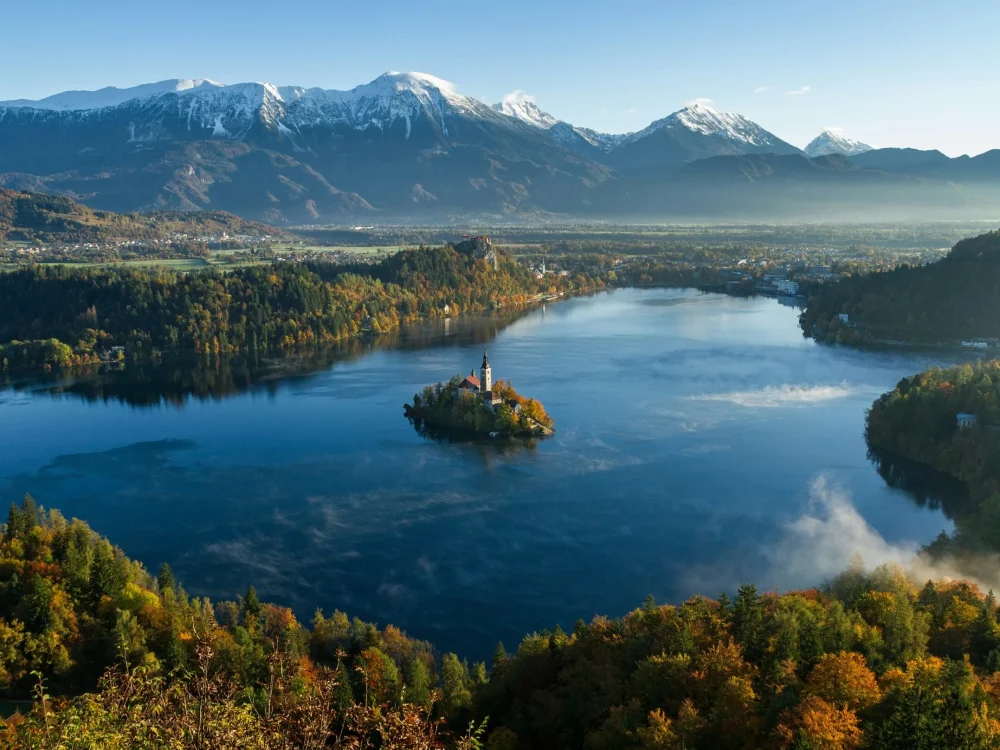 An aerial view of a picturesque lake surrounded by mountains and autumn foliage.