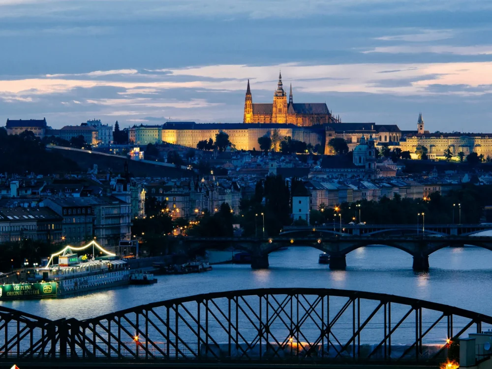 An evening cityscape of Prague with Charles Bridge and Prague Castle illuminated.